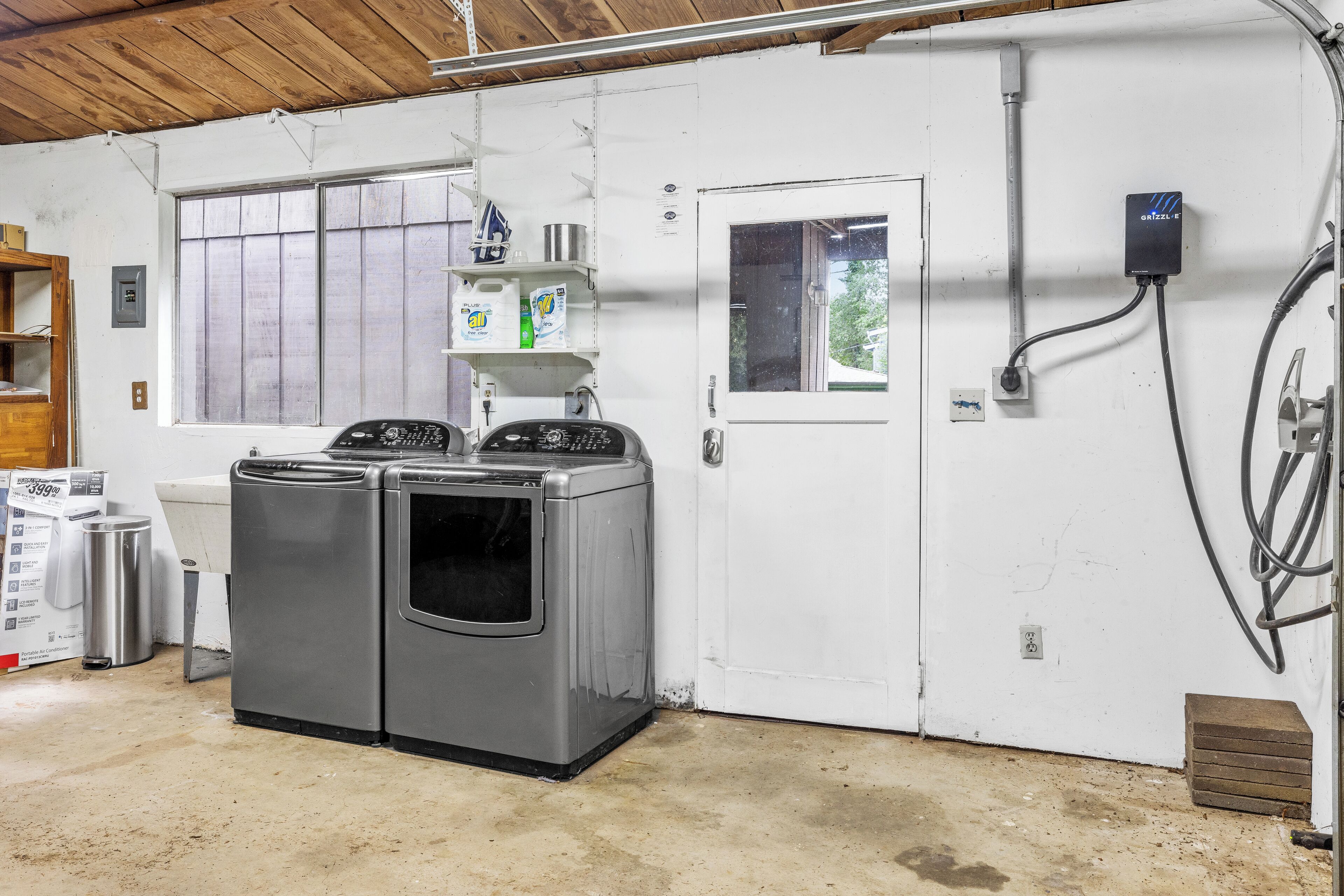 A laundry room with two stacked front-loading washers and dryers, a white door, a window, and a power outlet on the wall.