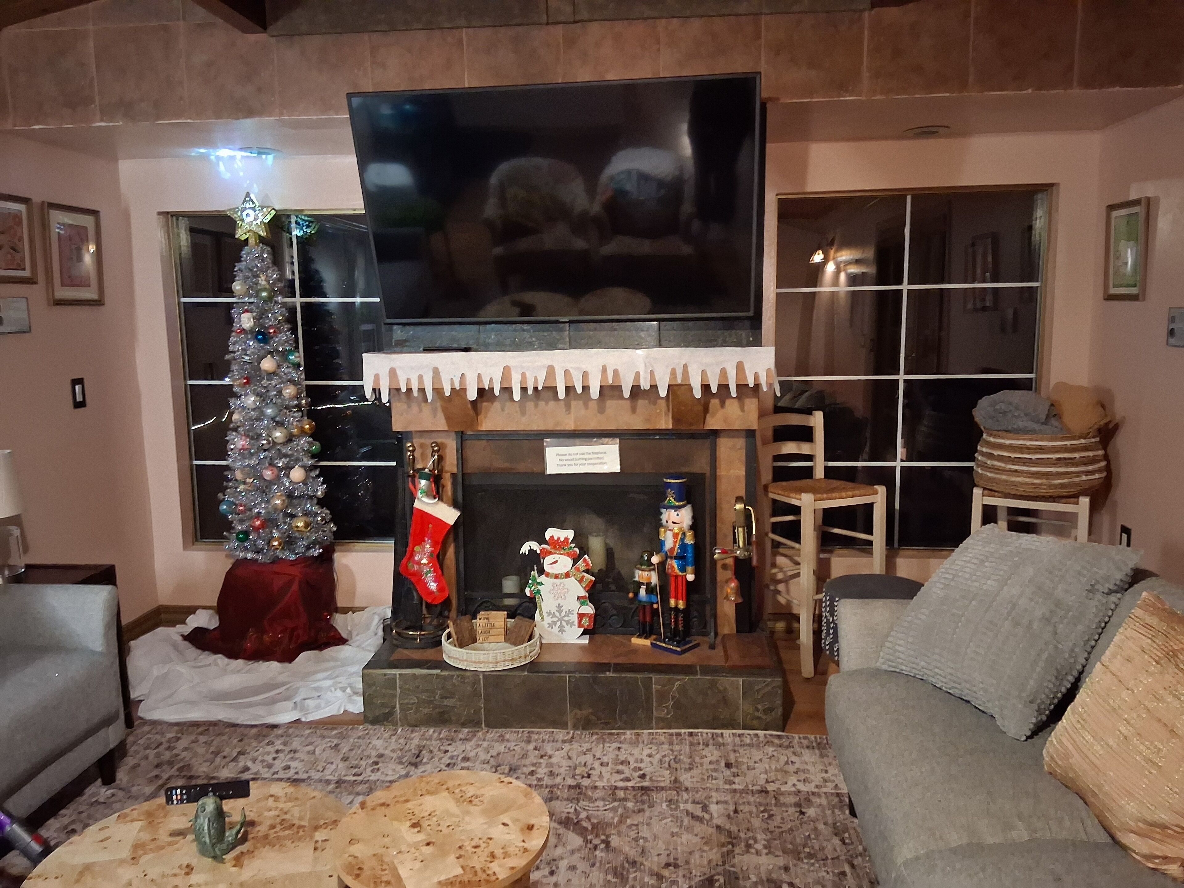 Un salon avec une cheminée, un téléviseur fixé au-dessus, un sapin de Noël et une figurine de casse-noisette.