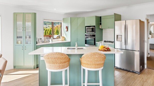 Una cocina moderna con armarios verdes, un refrigerador de acero inoxidable y una isla grande con dos taburetes de bar.