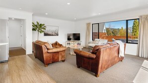 Una sala de estar moderna con dos sofás de cuero, un televisor, una mesa de centro y un ventanal con vistas a árboles y colinas.