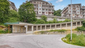 A multi-story residential building with balconies, a covered pedestrian walkway, and a curved road in front.
