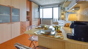 A compact kitchen with a dining area, featuring a coffee maker, a bowl of fruit, and a window providing natural light.