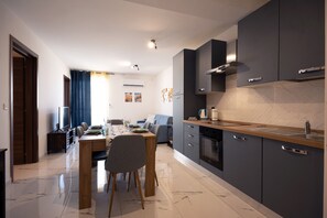 A modern kitchen with dark cabinets, a wooden countertop, and a dining area with a table and chairs. - Charming & modern 2 bedroom apartment DVAS1-1 (Msida)