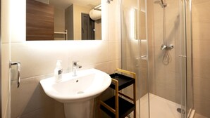 Ein modernes Badezimmer mit einer Duschkabine, einem Waschbecken mit Spiegel und einem hölzernen Ablagebrett.