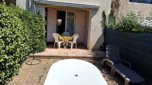 Un patio con una mesa y sillas, un área cubierta también con mesa y sillas, y un seto.