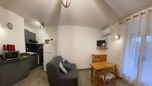 Un espacio habitable compacto con kitchenette, un sofá, una mesa de madera y un televisor.