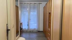Un pasillo con puertas de madera, un espejo y una ventana con cortinas traslúcidas.