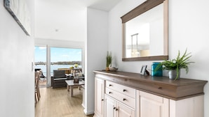 Un couloir doté d’un plancher en bois, d’une commode beige avec des tiroirs, d’un miroir et d’une vue sur un balcon aménagé avec du mobilier d’extérieur.