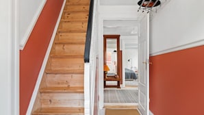 Een trap met houten treden die leidt naar een kamer met een bed, een nachtkastje en een lamp.