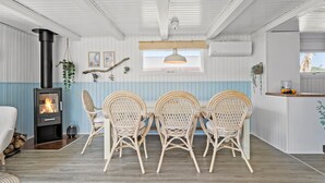 Um quarto aconchegante com lareira a lenha, cadeiras de vime, uma mesa de jantar e um lustre.