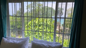 Ein Zimmer mit einem Fenster, das Gitterstäbe, zwei weiße Kissen und türkisfarbene Vorhänge zeigt.
