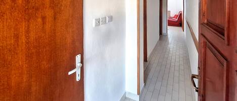 A hallway with a wooden door, white walls, and a tiled floor.