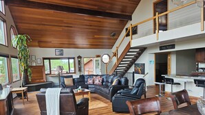 A spacious living area with a large L-shaped sectional sofa, a dining table, and a kitchen area with a bar. - Spacious Lodge in Charming Palmer with Incredible Mountain Views (Palmer)