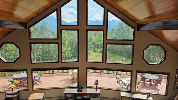 A spacious room with large windows offering mountain views, a wooden ceiling, and a cozy seating area with a table and chairs. - Spacious Lodge in Charming Palmer with Incredible Mountain Views (Palmer)