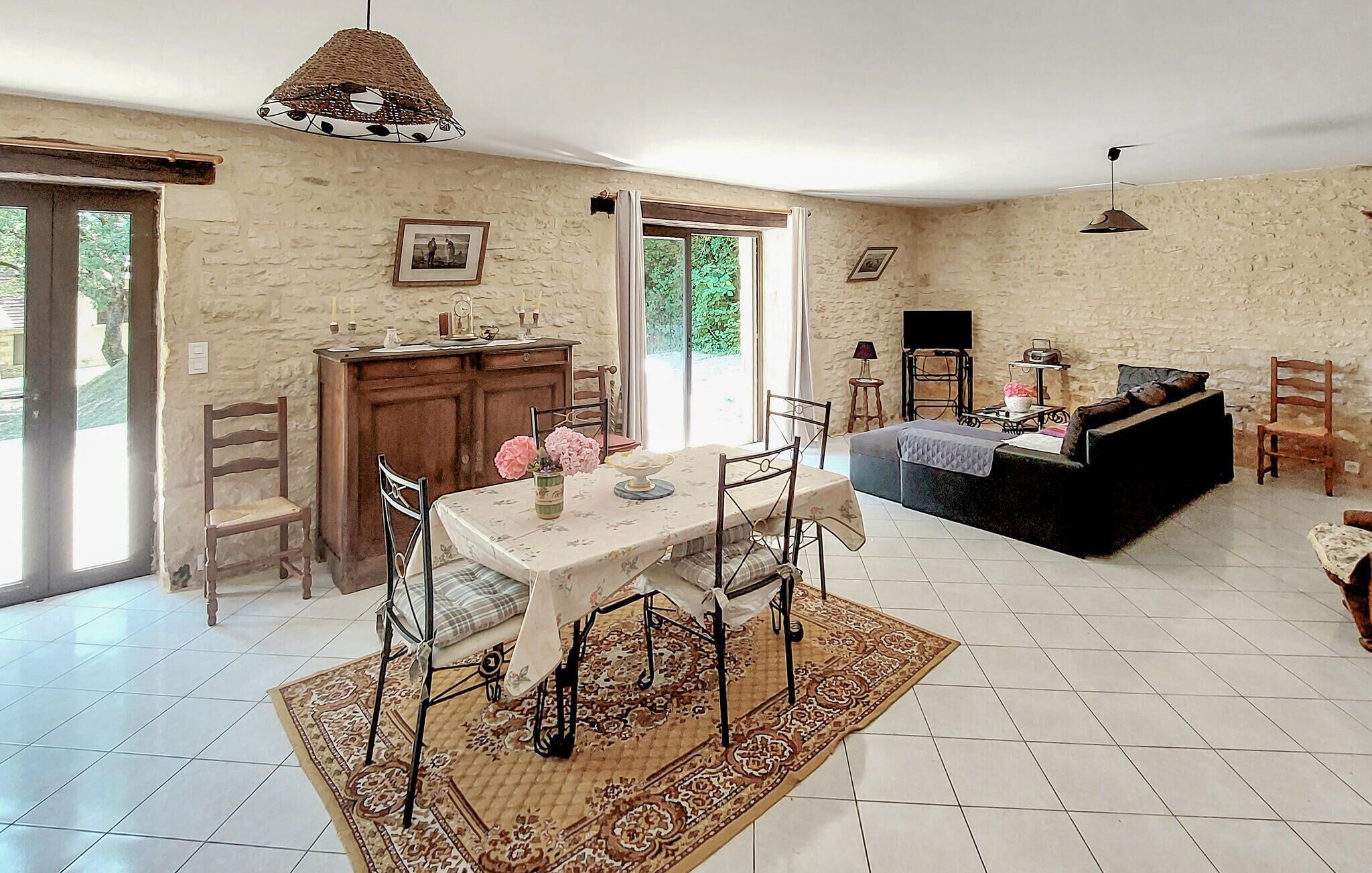 Un vaste espace de vie comprenant une table à manger, des chaises, un canapé et un téléviseur. Une grande fenêtre offre une belle vue sur la nature et permet à la lumière naturelle d’entrer.