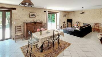 Un vaste espace de vie comprenant une table à manger, des chaises, un canapé et un téléviseur. Une grande fenêtre offre une belle vue sur la nature et permet à la lumière naturelle d’entrer.