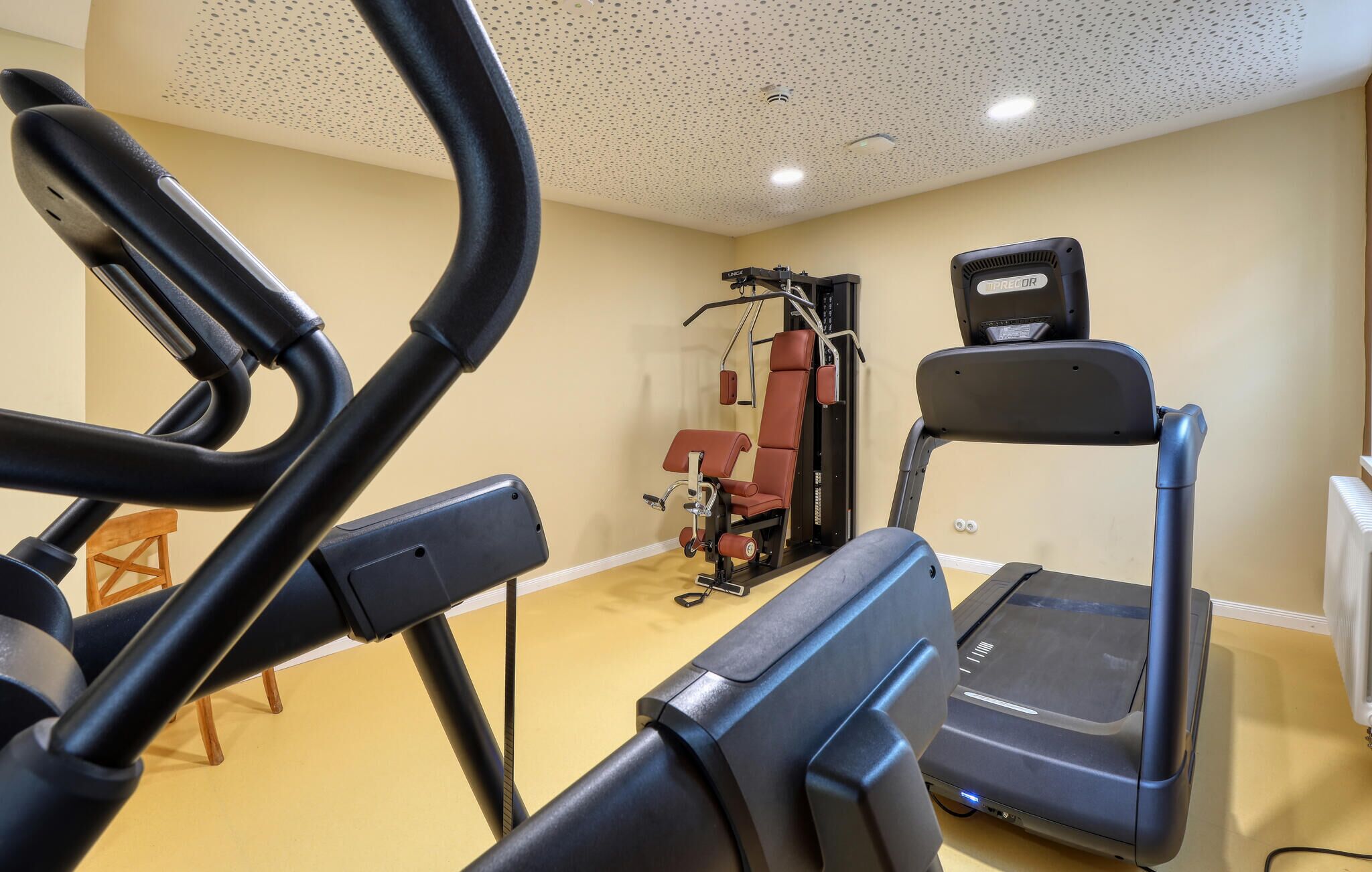 Une salle de sport équipée d’un tapis de course, d’un vélo elliptique et d’appareils de musculation.