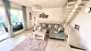 Una sala de estar moderna con un sofá modular, una mesa de centro, una escalera y un ventanal con cortinas.
