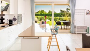 Una cocina moderna con una isla central, un comedor con sillas y vistas a un jardín a través de una puerta corrediza de vidrio.