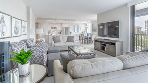 Ein modernes Wohnzimmer mit Sofa, Couchtisch und Fernseher. Im Hintergrund ist eine Essecke mit Tisch und Stühlen zu sehen.