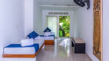 Two single beds with blue and white bedding, a bench, and a window offering a view of the surrounding greenery.