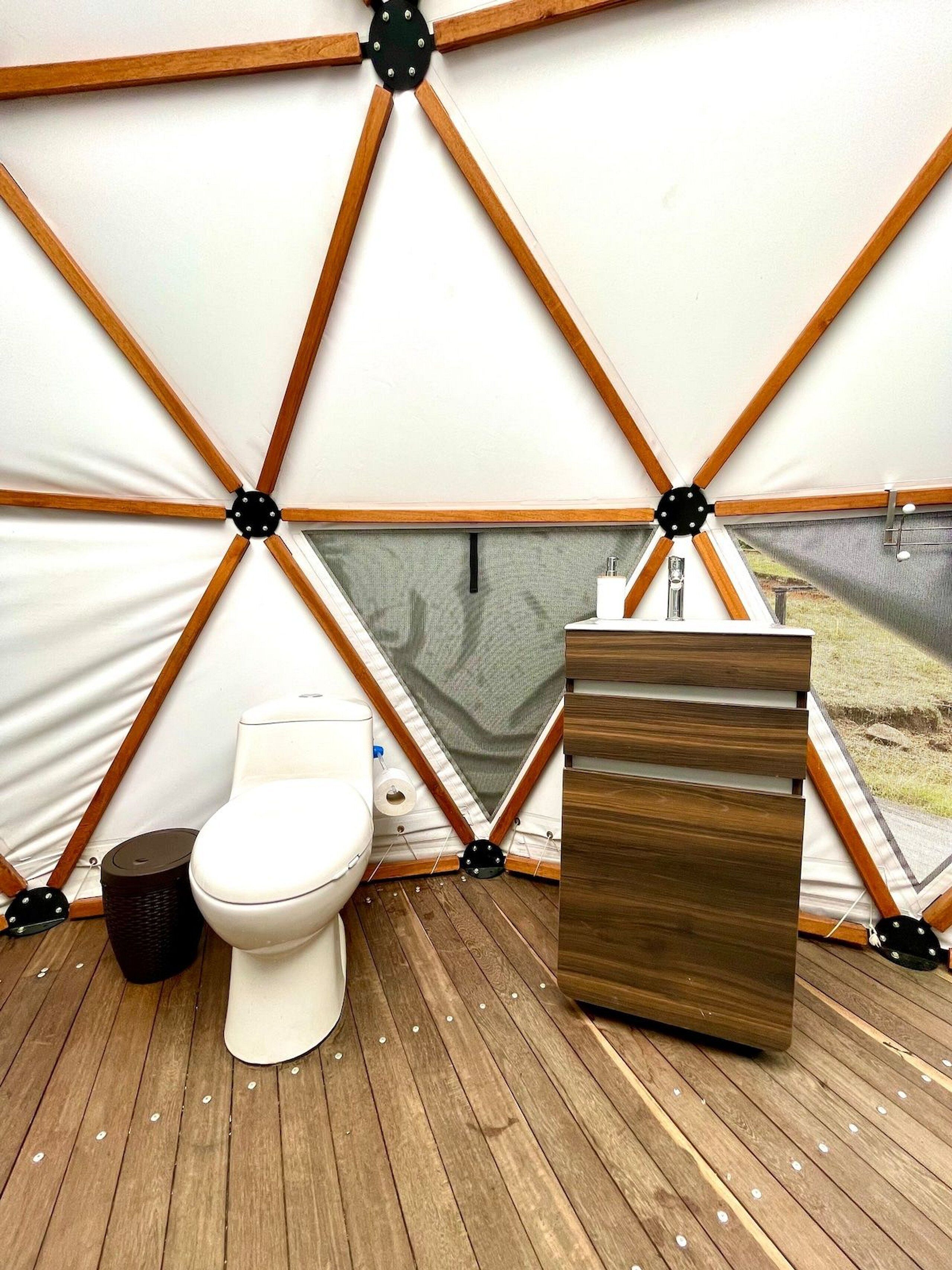 A tent with a wooden floor, a toilet, and a sink.