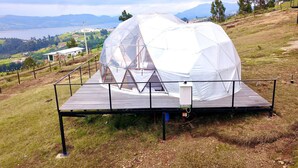 A geodesic dome structure on a wooden platform with a view of a lake and mountains in the background. - Glamping Spa con vista embalse de Tominé (Guatavita)