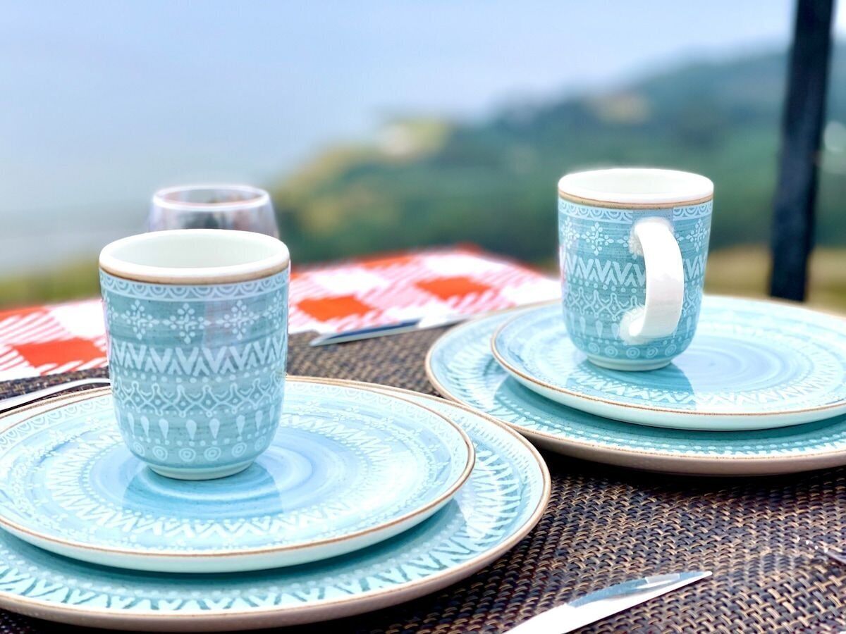 A table set with patterned blue and white ceramic plates and matching cups, with a clear view of the outdoors in the background.