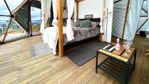 A cozy tented accommodation with a bed, a small table with a bottle and glasses, and a view of the outdoors. - Glamping Spa con vista embalse de Tominé (Guatavita)