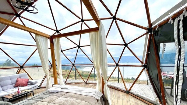 A geodesic dome room with a bed, a sofa, and a view of the landscape. - Glamping Spa con vista embalse de Tominé (Guatavita)