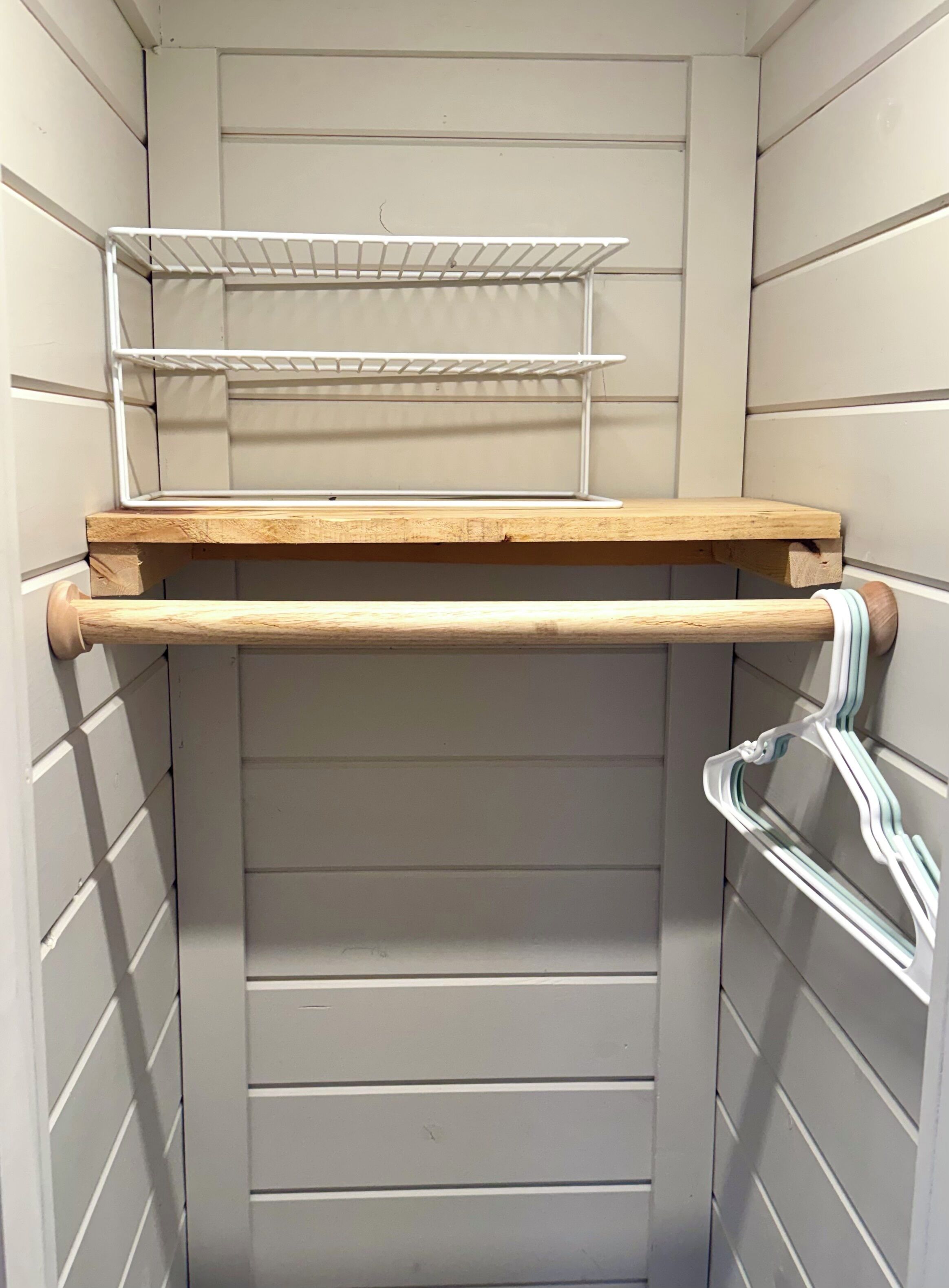 A storage closet with a wooden shelf, a metal rack, and a white pipe.