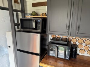 A compact kitchen with a stainless steel refrigerator, a microwave, a toaster, and a coffee maker. - Shangri-La Tiny Home with WiFi near Winery, Lakes, and Antique Shops!! (Azle)