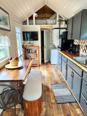A compact kitchen with a dining area, a built-in TV, and a small refrigerator. - Shangri-La Tiny Home with WiFi near Winery, Lakes, and Antique Shops!! (Azle)