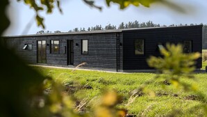 Un bâtiment moderne, aux lignes épurées, avec une façade en bois sombre, de grandes fenêtres et un toit plat, entouré de verdure.