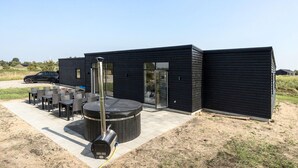 Un bâtiment moderne de couleur noire doté d’un patio comprenant un jacuzzi, des sièges d’extérieur et un barbecue.
