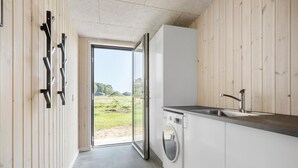 Une cuisine moderne équipée d’un lave-linge intégré, d’un évier et d’une grande fenêtre donnant sur un espace extérieur verdoyant.