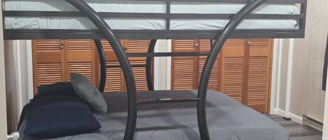 Ein Stockbett mit kreisförmigem Gestell, einem Holz-Kopfteil und einer grauen Matratze.