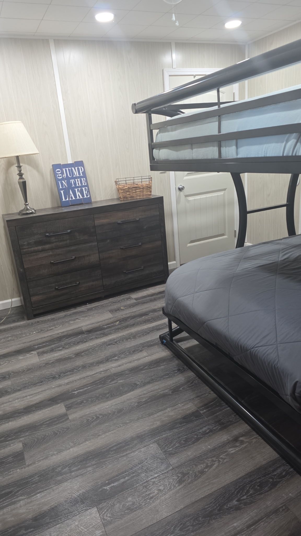 A bedroom with a bunk bed, a dresser, a lamp, and a sign on the wall.