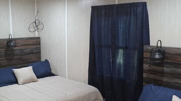 Habitación de hotel con dos camas, cabecero de madera, cortina oscura y una tetera en la mesita de noche.