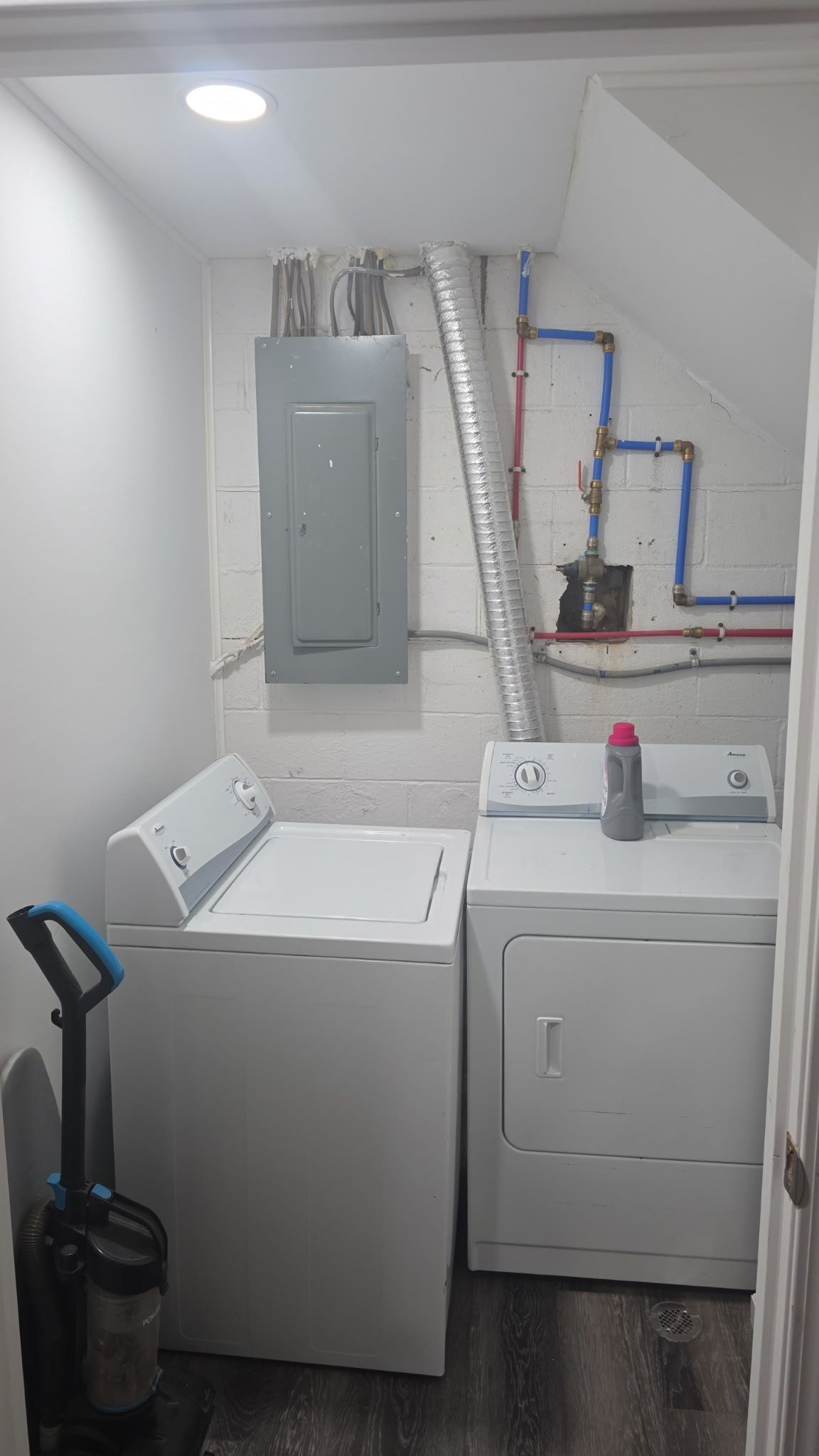 A laundry room with two washing machines, a vacuum cleaner, and visible plumbing.