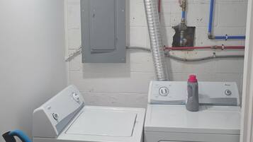 A laundry room with two washing machines, a vacuum cleaner, and visible plumbing.
