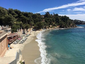 A beach with a row of sun loungers and umbrellas, a building with a balcony overlooking the beach, and a clear view of the sea. - Apartment with terrace and sea view near Rayol Beach (Rayol-Canadel-sur-Mer)