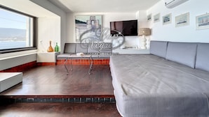 A modern living room with a grey sofa, a small table, and a TV. There is a window with a view of the sea. - Waterfront house with a rooftop and private dock in Cavalière (Le Lavandou)