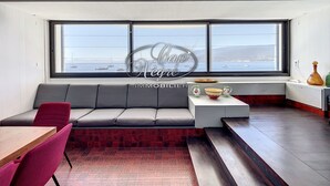 A modern interior with a large window, a sofa, a dining table, and a small kitchen area. - Waterfront house with a rooftop and private dock in Cavalière (Le Lavandou)