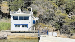 A waterfront property with a white building, a dock, and a rocky hillside. - Waterfront house with a rooftop and private dock in Cavalière (Le Lavandou)