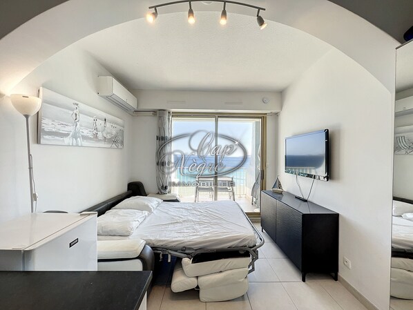 A modern bedroom with a bed, a desk, a TV, and a balcony with a view.