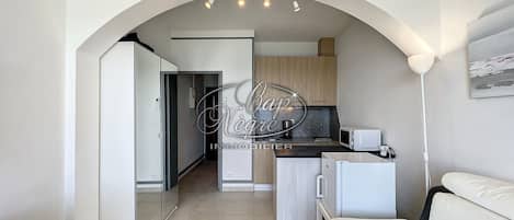 A compact living space with a kitchenette, a sofa, and a hallway leading to a door.