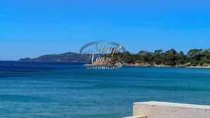 A coastal view with a clear sky, a boat on the water, and a rocky shoreline with trees.