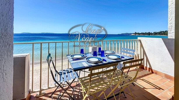 A balcony with a table set for dining, overlooking a beach and the sea.