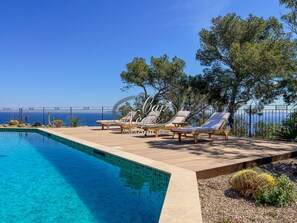 A swimming pool with lounge chairs, a clear view of the sea, and a fenced patio area. - Prestigious property with a pool and panoramic sea view in Cap Nègre (Le Lavandou)